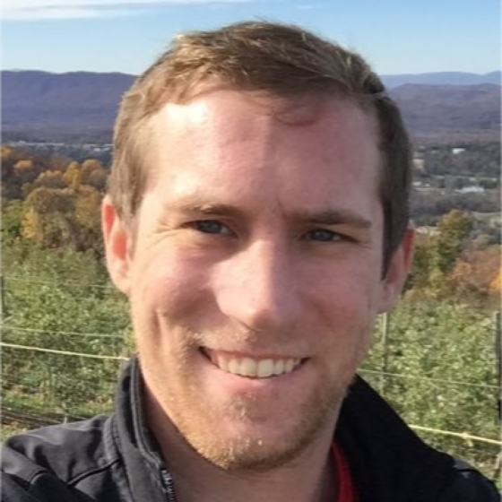 Jake Selby smiling outdoors with mountains in the background